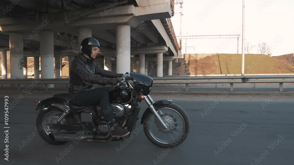 Young man riding motorcycle on the road under the bridge at sunset, slow motion Young man riding motorcycle on the road under the bridge at sunset, slow motion