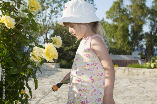 Girl wearing sunhat watering roses photo