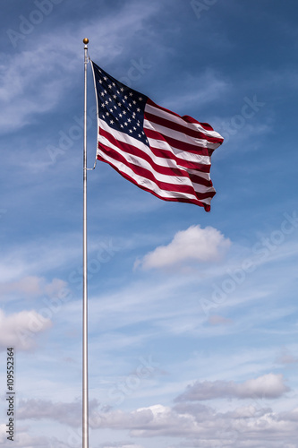 Single American Flag with a cloudy blue sky background.