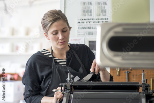 Female letterpress printer inking machine in workshop