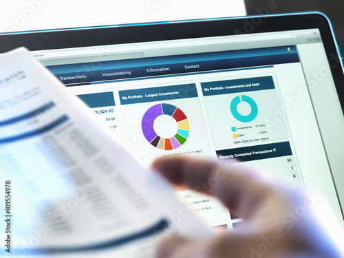 Investor checking performance of financial portfolio online whilst reviewing investment statement