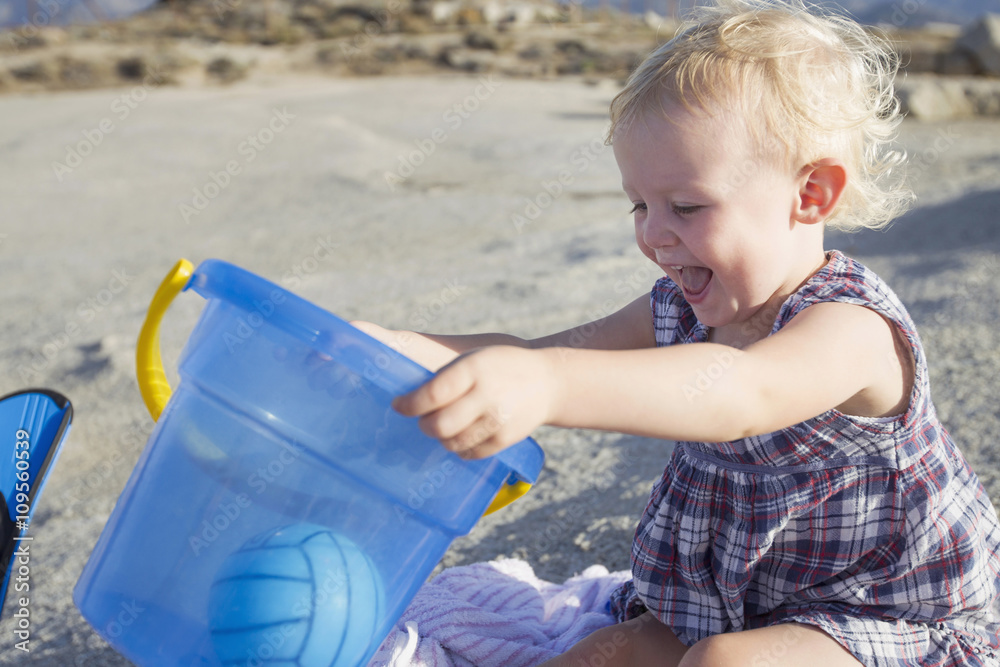 Happy female toddler playing on beach with toy bucket Happy female toddler playing on beach with toy bucket