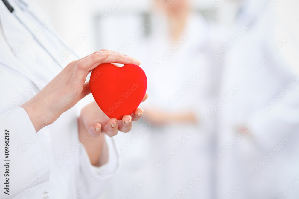 Female doctor with stethoscope holding heart. Two doctors standing in the background Female doctor with stethoscope holding heart. Two doctors standing in the background