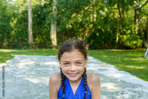 Portrait of girl in garden, slip n slide water mat behind her