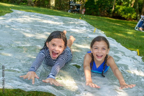 Two girls sliding on slip n slide water mat in garden photo