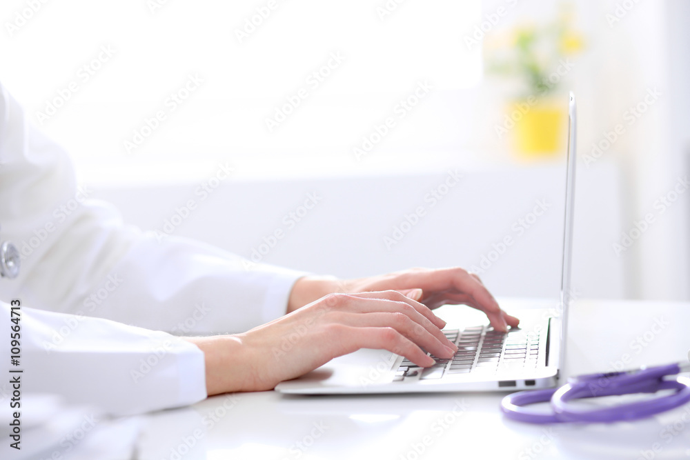 Close-up of female doctor typing laptop sitting at a table in the hospital Close-up of female doctor typing laptop sitting at a table in the hospital