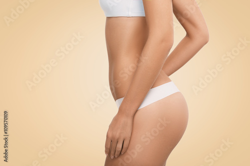 Side view of perfect female body in white lingerie. Young woman wearing white underwear posing isolated against blank wall background with copy space for your text message or advertising content