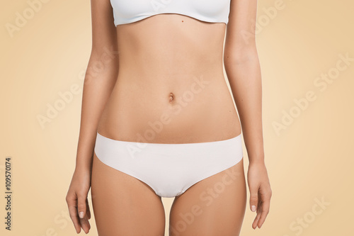 Cropped isolated portrait of young and beautiful female body standing against blank wall. Close up view of attractive woman in great shape wearing white underwear posing against studio background