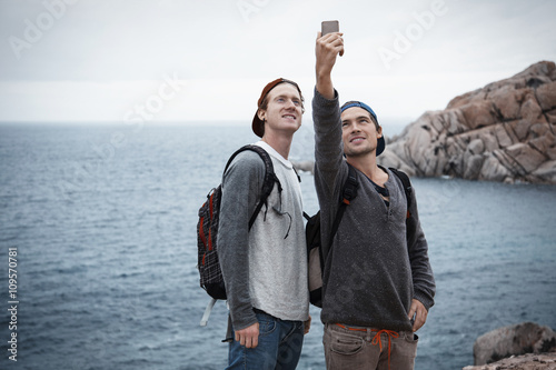 Young men in front of ocean using smartphone to take selfie photo