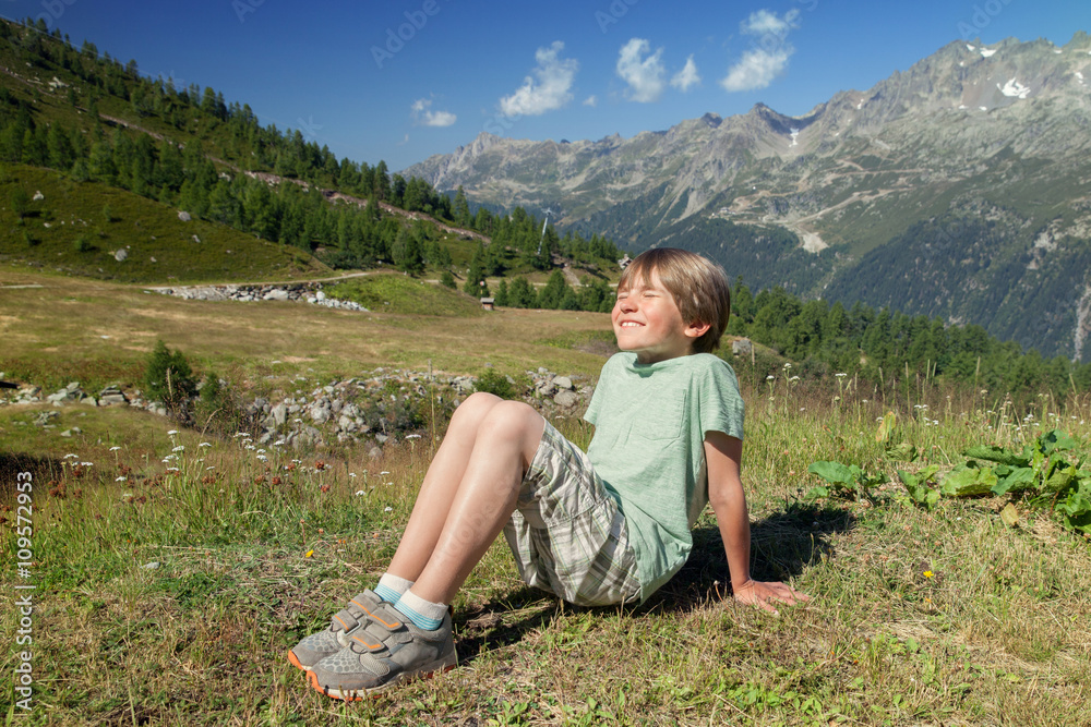 Naklejka premium The happy six years boy blinks in sunlights on mountain slope