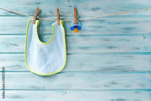 Baby bib and pacifier hanging on a clothesline on wooden background