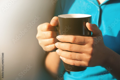 Hands of woman holding a ceramic cup.