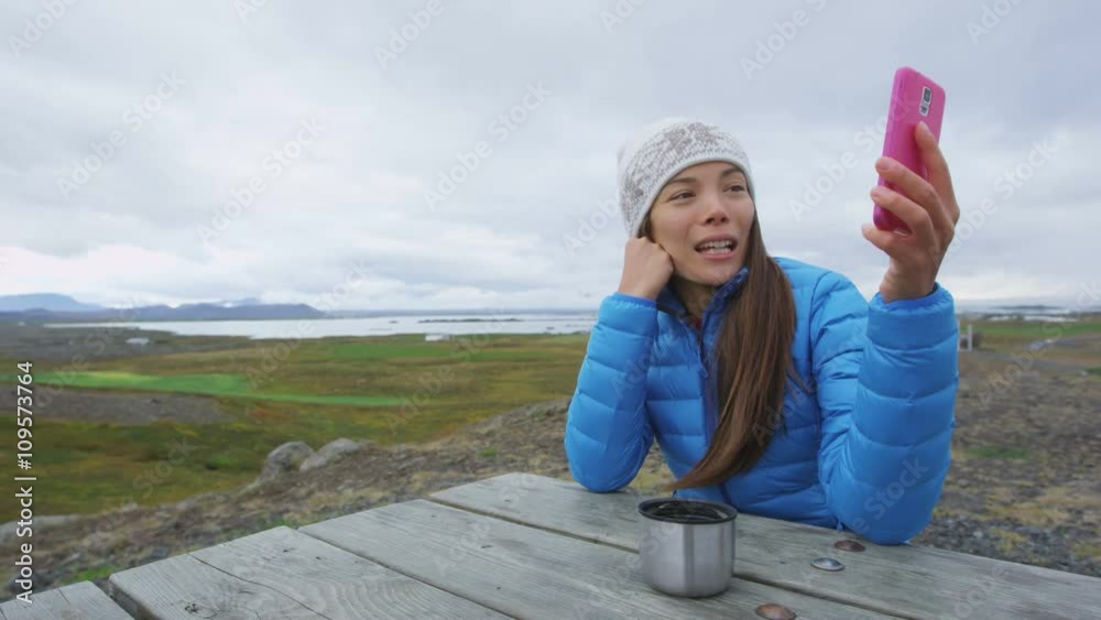 Video chat conversation - Woman on smart phone talking in nature outdoor using smartphone app drinking coffee outside. Mixed race Asian Chinese Caucasian woman in active lifestyle on Iceland.