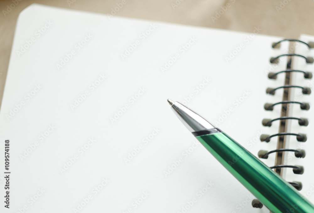 A part of open blank white notebook and green pen on the desk A part of open blank white notebook and green pen on the desk