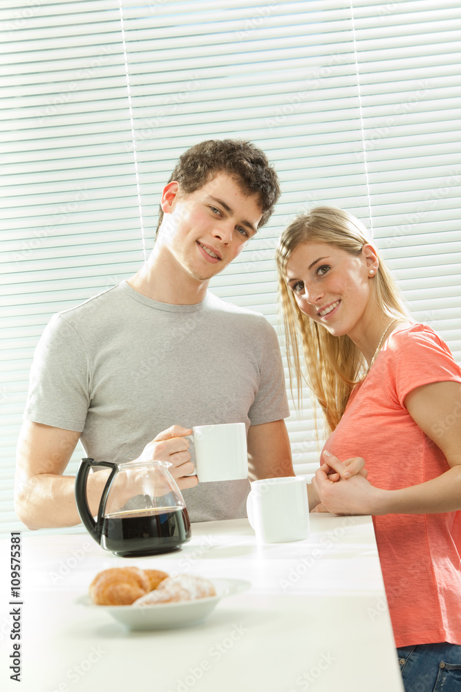 Young casual couple have breakfast with coffee and croissant with venetian blind window