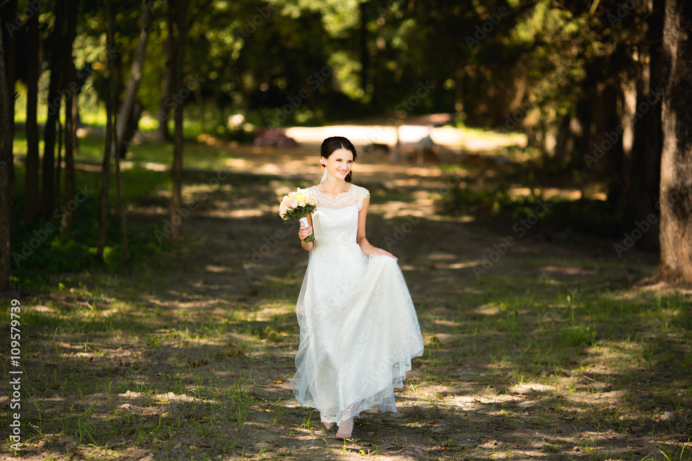 Beautiful sensual young brunette bride walking in forest holding bouquet outdoor on natural background. Magic full length photo Beautiful sensual young brunette bride walking in forest holding bouquet outdoor on natural background. Magic full length photo
