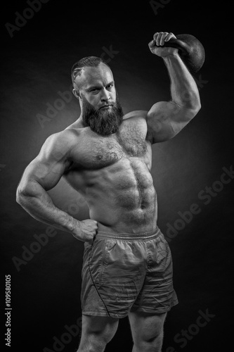 Bodybuilder with a beard lifts a heavy kettlebell.