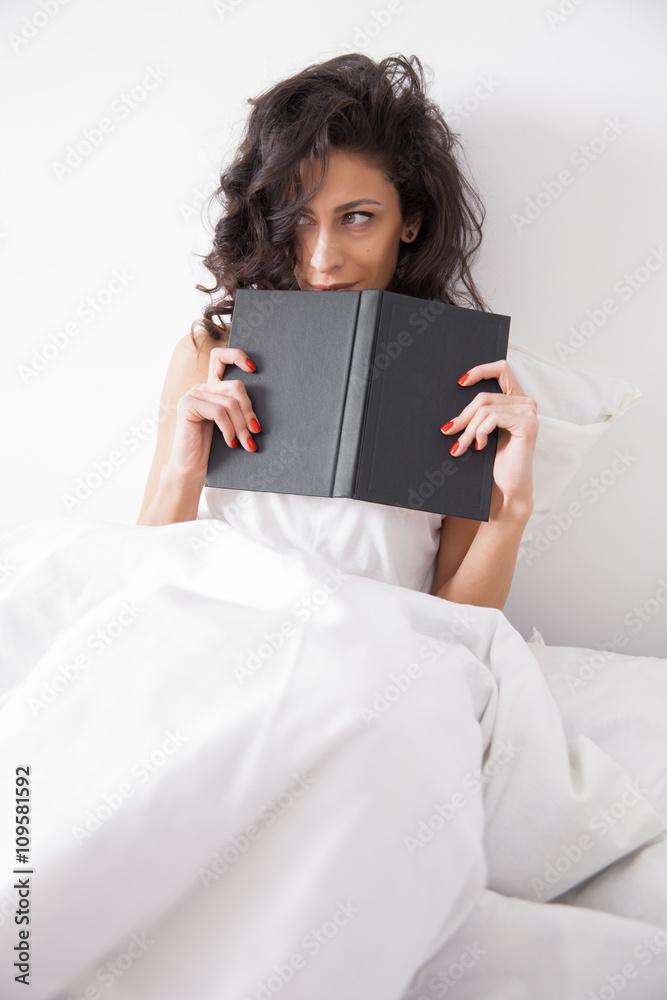 Brunette long hair woman under the duvet reading a book Brunette long hair woman under the duvet reading a book