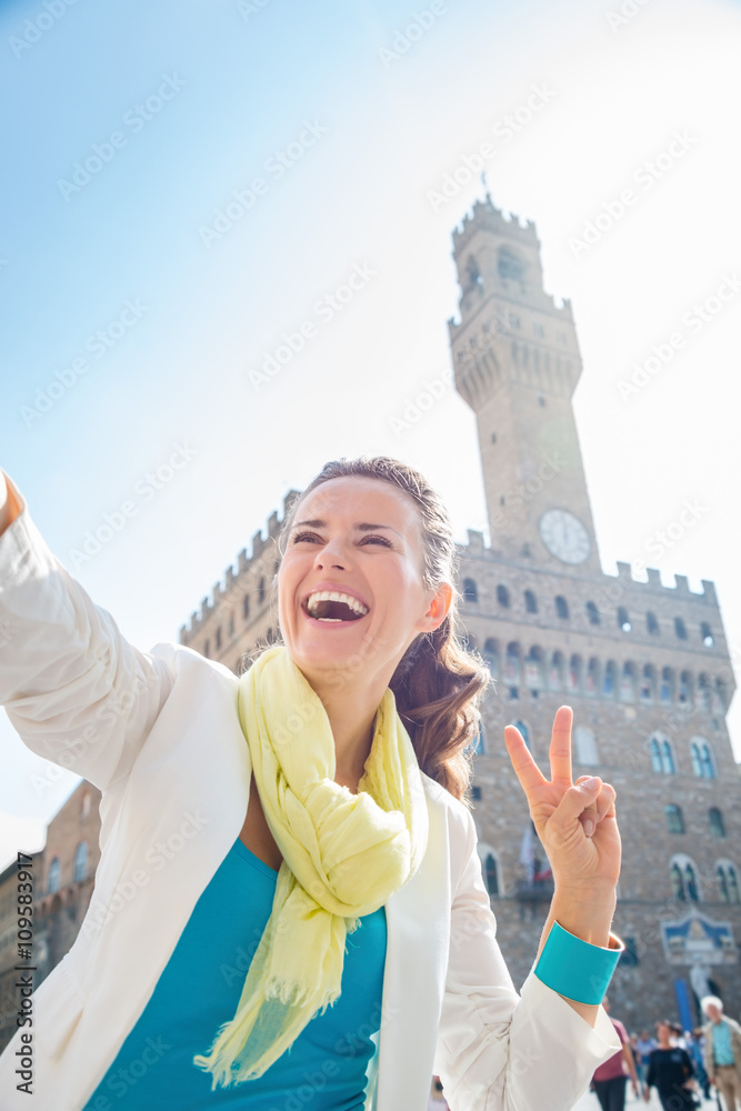 Fototapeta premium Woman showing victory and taking selfie near Palazzo Vecchio