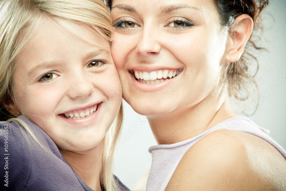 Beautiful brunette woman with young blond girl on grey background Beautiful brunette woman with young blond girl on grey background