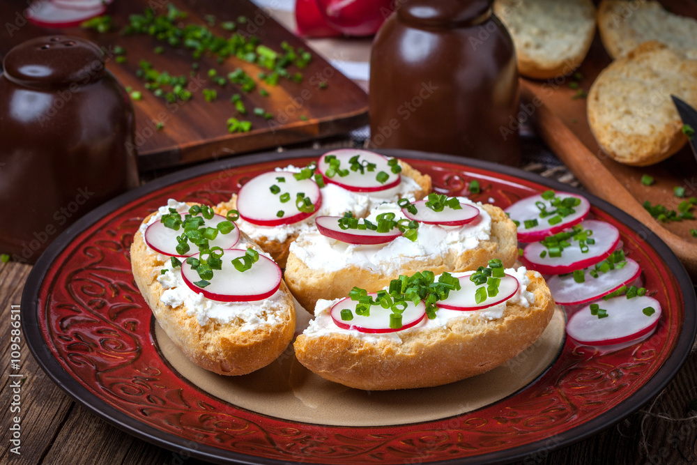 Toasts with radish, chives and cottage cheese on a wooden table.