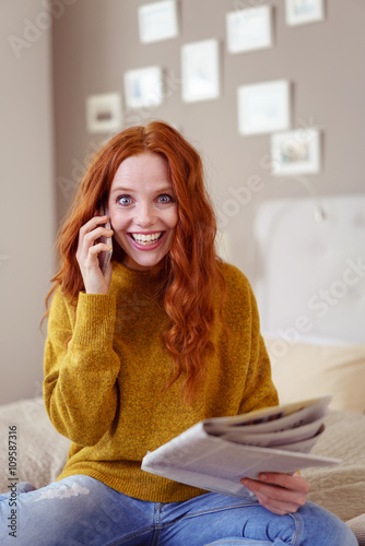 lachende frau mit handy und tageszeitung zu hause photo