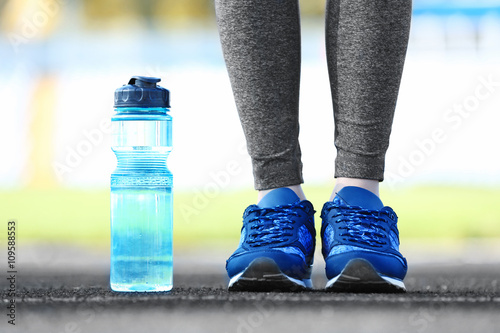 Woman in sports clothes and sneakers with bottle outdoors