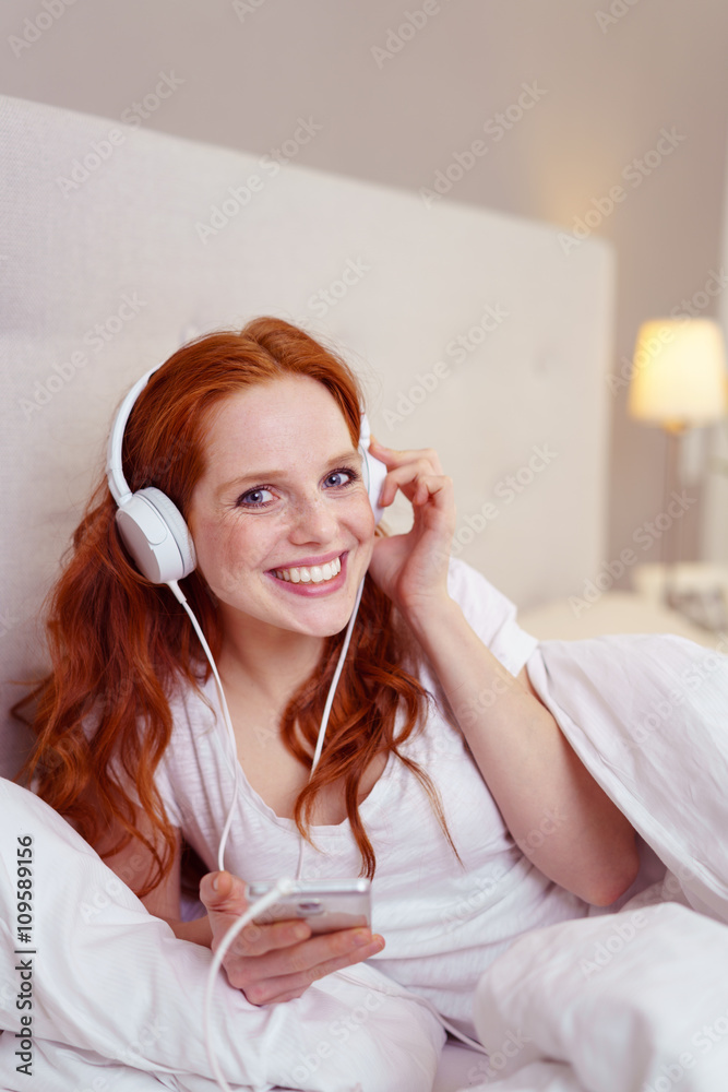 Naklejka premium frau liegt im bett und hört musik mit ihrem mobiltelefon
