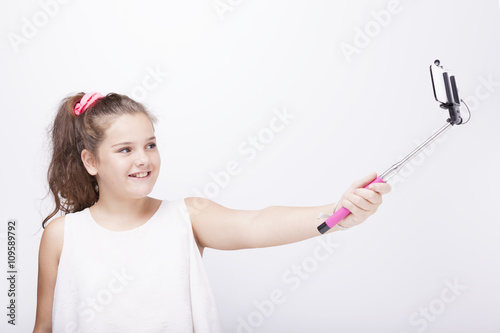 Little girl using a selfie stick on grey background