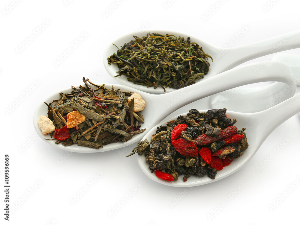 Fototapeta premium Different sorts of dry tea in ceramic spoons, isolated on white