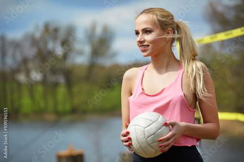 Joyful sexy blond girl playing volleyball outdoors on the lakesi