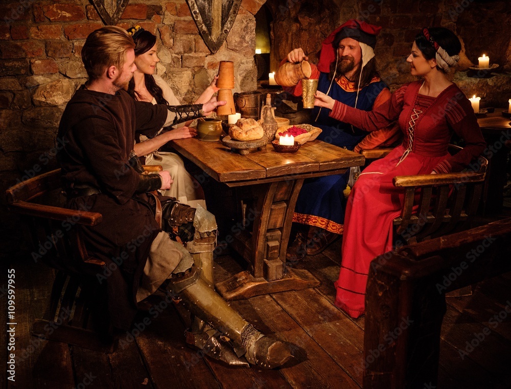 Medieval people eat and drink in ancient castle tavern.