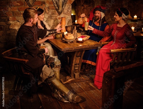 Medieval people eat and drink in ancient castle tavern.