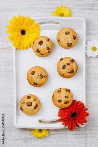 Homemade chocolate chip muffins on a white wooden tray decorated with flowers.