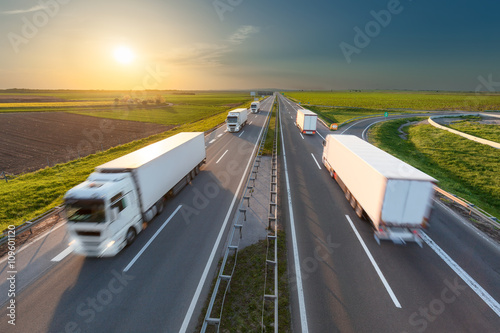 Big white trucks on highway towards the setting sun