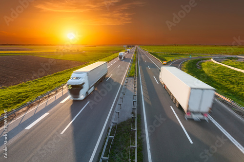 Delivery transport trucks on the empty highway at sunset
