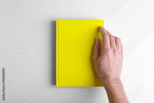 Male hand hold the yellow book on white table.