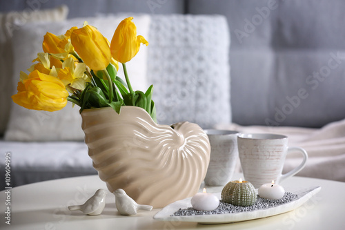 Beautiful fresh flowers in vase, cups and candles on white table, indoors