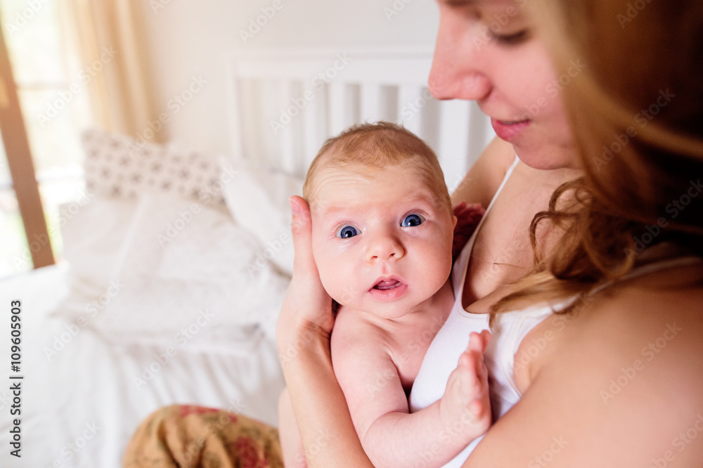 Young mother holding her newborn baby son, home bedroom Young mother holding her newborn baby son, home bedroom