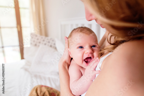 Young mother holding her newborn baby son, home bedroom