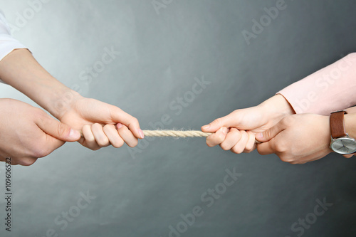 People hands pulling rope for playing tug of war on grey background