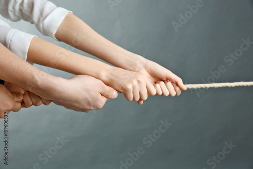 People hands pulling rope for playing tug of war on grey background