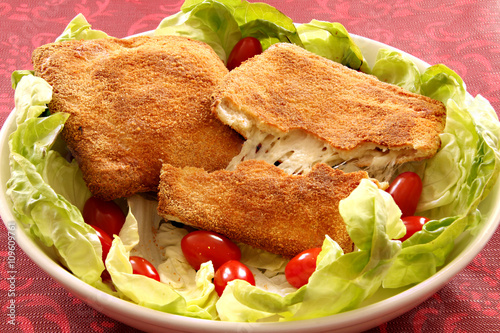 A dish with baked stringy mozzarella in carrozza with green salad and tomatoes cherry. Red background.