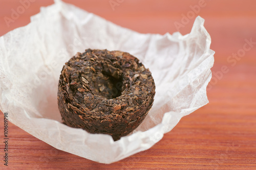 Unpacked dry pressed pu erh tea leaves briquette closeup on red wooden table