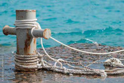 Photography Rusty mooring bollard with ship ropes and  clear turquouse sea ocen water on bac
