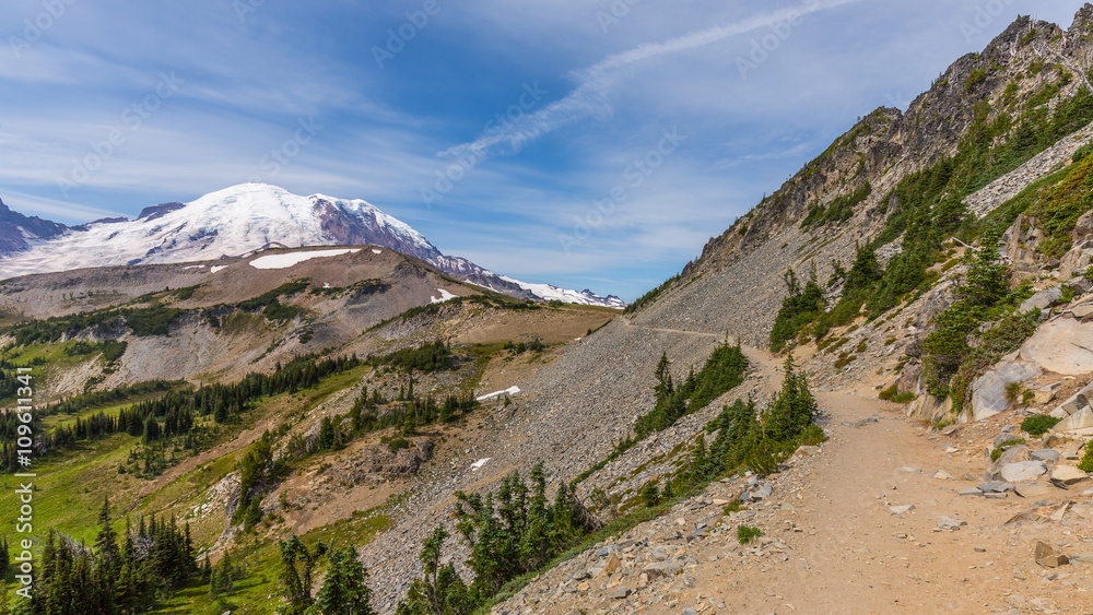 Amazing view at the snowy peaks which rose against the blue of a cloudless sky. Narrow rocky trail high in the mountains.BERKELEY PARK TRAIL, Sunrise Area, Mount Rainier National Park