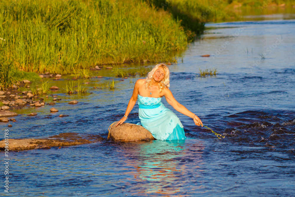 Fototapeta premium Mature beautiful blonde in blue dress enjoying the water