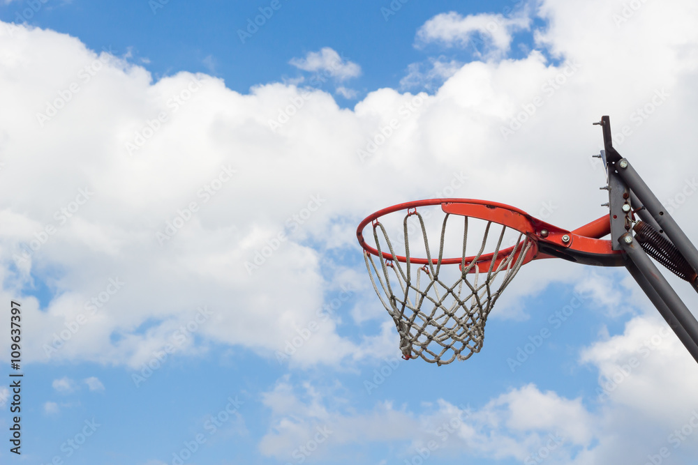 Basketball hoop against fluffy clouds and blue sky