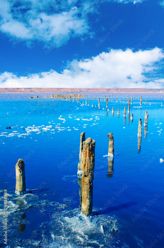 Beautiful salt lake with blue and pink water, white clouds and wooden posts, natural landscape amazing background Beautiful salt lake with blue and pink water, white clouds and wooden posts, natural landscape amazing background