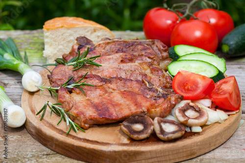 Grilled pork meat with mushrooms and fresh vegetable salad on wooden board